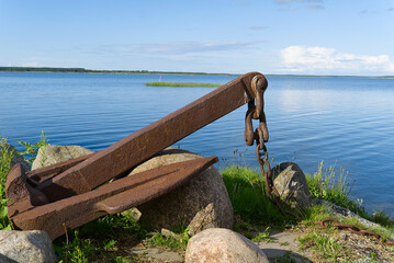 Large rusty old anchor on rocky baltic sea shore.