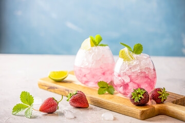 Pink cocktail with lime, crushed ice, strawberries and mint on the light background, selective focus image, copy spice for you text, summer vacation and party concept.