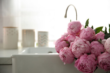 Bouquet of beautiful pink peonies in kitchen sink. Space for text