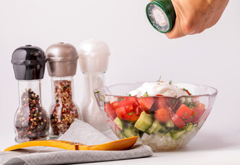 The woman adds seasoning to the salad.