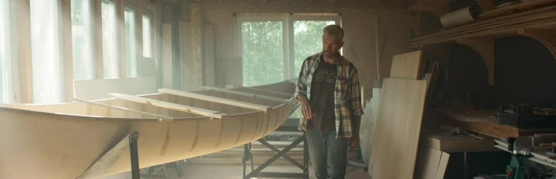 Caucasian male building a traditional wooden canoe in his workshop. Boat making hobby, small business owner. Shot on RED Dragon