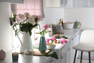Beautiful peonies in vases on kitchen counter