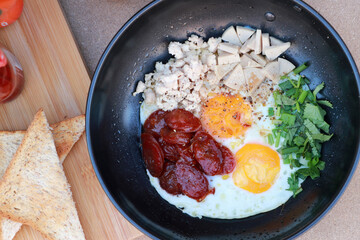 pan fried egg with toppings, Chinese sausage and pork sausage in the black pan with slice of bread.