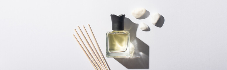 top view of aroma sticks with perfume in bottle near stones on white background, panoramic shot