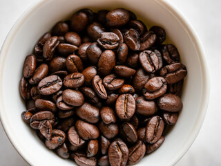 Top-down view of roasted coffee beans in a white cup on a white background