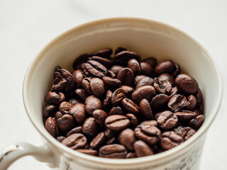 High angle view of roasted coffee beans in a white porcelain cup on a white background