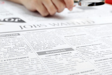 Obraz premium Woman looking through magnifying glass at newspaper, closeup. Job search concept