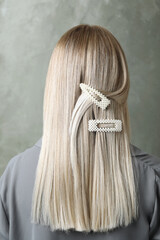 Young woman with beautiful hair clips on grey background, back view