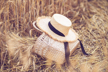 Modern fashion concept with straw hat, bag on wheat field.