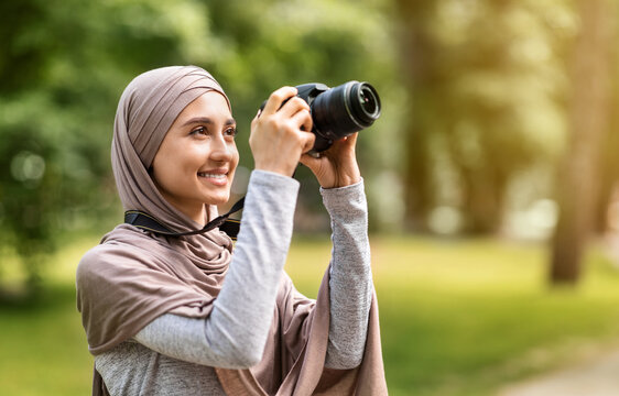 Girl in hijab taking photos with professional camera at park