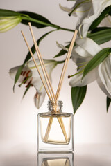 selective focus of wooden sticks in perfume in bottle near lily flowers on beige background