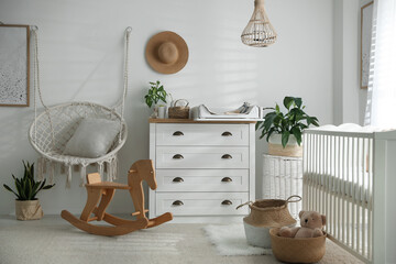 Chest of drawers with changing tray and pad near comfortable cradle in baby room. Interior design © New Africa