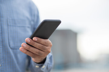 Close up male hands holding using black smartphone on city background.