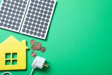 Flat lay composition with solar panels, house model and coins on green background. Space for text