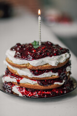 Homemade sugar free sponge cake with mascarpone filling and forest fruits sauce with birthday lighted candle on top.