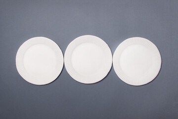 three white eco-friendly cardboard plates lie on gray colored paper background. Top view. Close-up. Mock-up