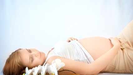 Obraz na płótnie Canvas Pregnant woman practicing breathing prenatal exercises with beautiful flowers orchids on white background. Relaxation and delivery preparation mindfulness concepts. Sports concept.