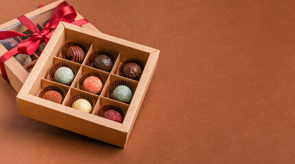 Chocolate sweets from various chocolate toppings in a box a satin ribbon brown background. The concept festive dessert.