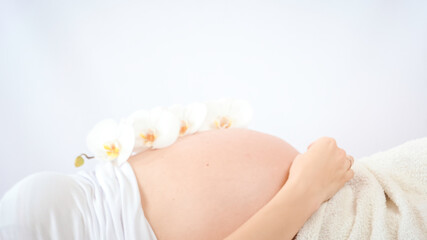 Obraz na płótnie Canvas Pregnant woman practicing breathing prenatal exercises with beautiful flowers orchids on white background. Relaxation and delivery preparation mindfulness concepts. Sports concept.