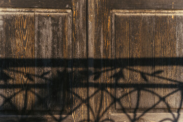 Ancient Weathered Wooden Doors with Shadow of Ornate Iron Fence