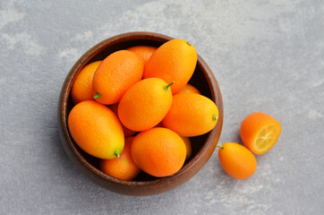 Raw organic kumquat citrus fruits in wooden bowl on concrete background. Healthy vegetarian food. Top view.
