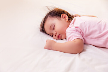 Fototapeta na wymiar Adorable innocent baby girl sleeping on bed with good dream. Cute mixed race infant baby get deep sleep and peaceful. Lovely toddler girl wear pink baby dress. Child has lovely face. copy space