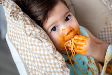 Adorable little toddler girl or infant baby eating delicious spaghetti food with tomato sauce on...