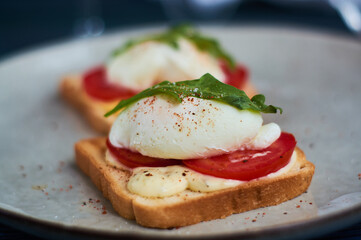 Large gray ceramic plate with toast and poached eggs, greens, tomatoes, sauce. Tasty breakfast. Glasses of wine.