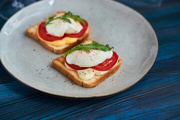 Fototapeta na wymiar Tasty home breakfast of square toast with sliced fresh tomato and egg benedict with urugula.