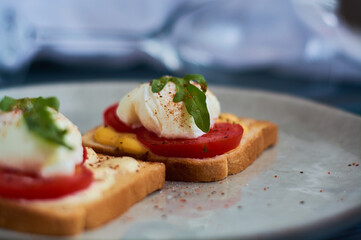 Large gray ceramic plate with toast and poached eggs, greens, tomatoes, sauce. Tasty breakfast. Glasses of wine.