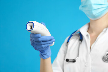 Doctor holding non contact infrared thermometer against light blue background, focus on hand....