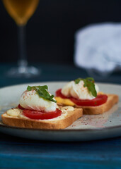 Large gray ceramic plate with toast and poached eggs, greens, tomatoes, sauce. Tasty breakfast. Glasses of wine.