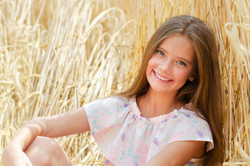 Portrait of smiling cute little girl child sitting on field of wheat - 364742373
