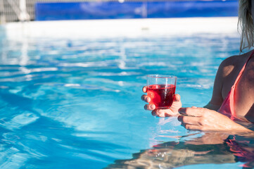 Woman's hand holds a glass with a drink while taking a bath in the pool.Copy space.Enjoying vacations