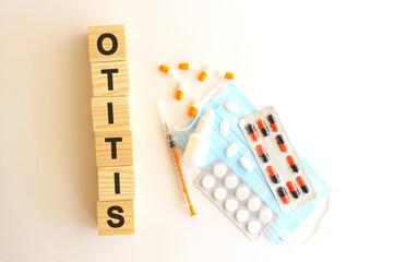 The words OTITIS is made of wooden cubes on a white background with medical drugs and medical mask. Medical concept.