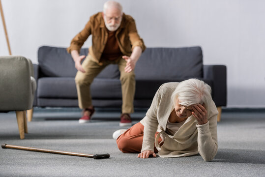 selective focus of senior man hurrying to help wife lying on floor near walking stick
