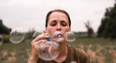 The girl blows soap bubbles. A young woman sits in nature and blows soap balls. The person in front.