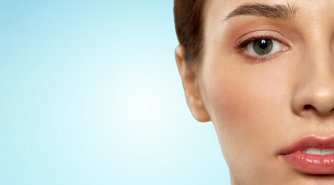 beauty, makeup and vision concept - close up of beautiful young woman face and eyes over blue background