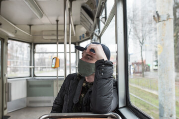 Male wearing face mask inside public transport watches at the window with rainy weather
