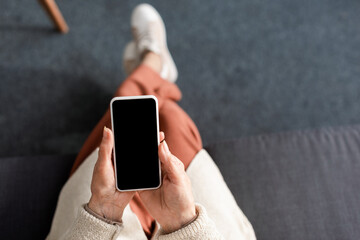 top view of senior woman sitting and holding smartphone with blank screen