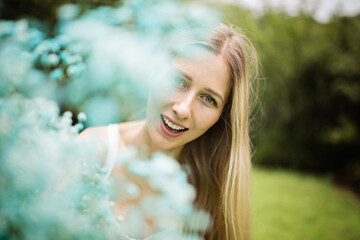 Naklejka premium Portrait of beautiful blonde woman with bouquet of blue flowers. Young woman walking alone in the summer park after covid-19 coronavirus pandemic quarantine. Health care and happiness concept.