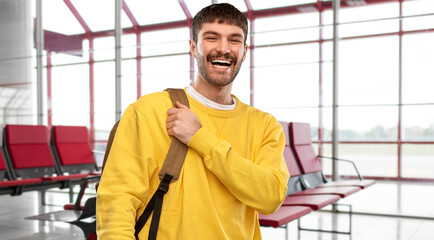 travel, tourism and people concept - happy smiling young man with backpack over airport terminal background