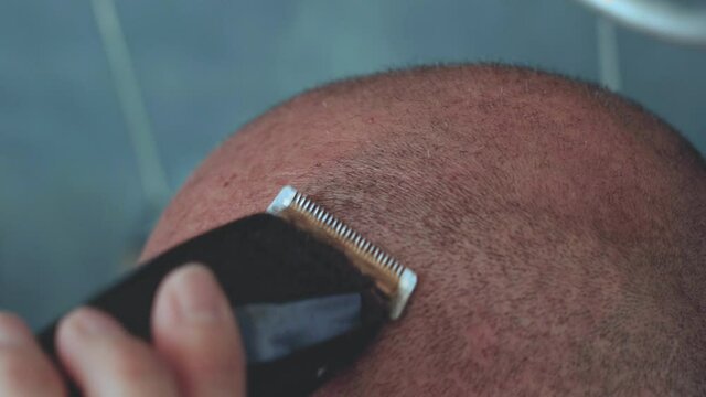 Close up of a caucasian bald man shaving his head with electric razor.