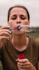 The girl blows soap bubbles. A young woman sits in nature and blows soap balls. The person in front.