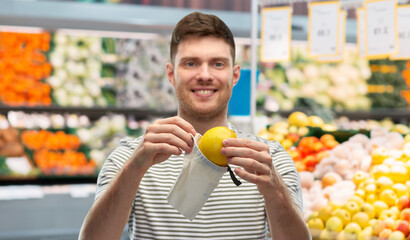food, sustainability and eco living concept - smiling young man in striped t-shirt with lemon in reusable canvas bag over grocery store or supermarket background