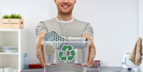 metal recycling, waste sorting and sustainability concept - smiling young man in striped t-shirt holding plastic box with tin cans over home kitchen background - Powered by Adobe