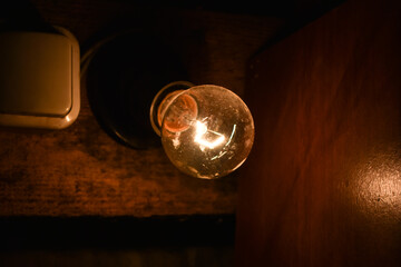 Light bulb next to the switch on the wall in a dark room.  Close up vintage glowing light bulbs, Edison's lamp on the dark background with copy space. Bright idea concept.