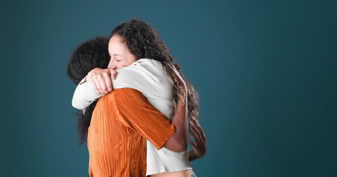 Beautiful black and brunette woman with curly hair hugging affectionately on blue background