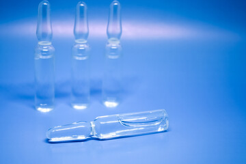 Transparent medical ampoules close-up, selective focus. A lot of glass ampoules on a blue background. Medical concept. Space for text
