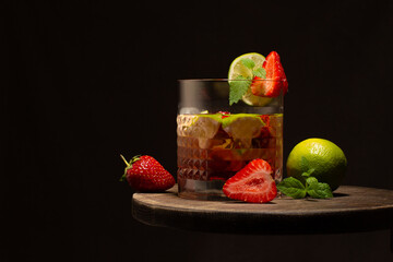 Strawberry and lime coktail in crystal glass with ice cubes and mint leaves on wooden table.Close up.